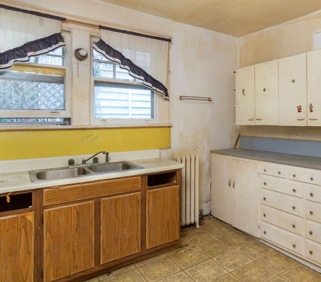 Kitchen before: worn wood base cabinets, old sink and stained walls