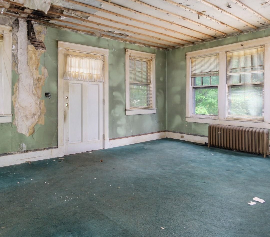 Living room before: ceiling open to the joists, damaged plaster and old carpet
