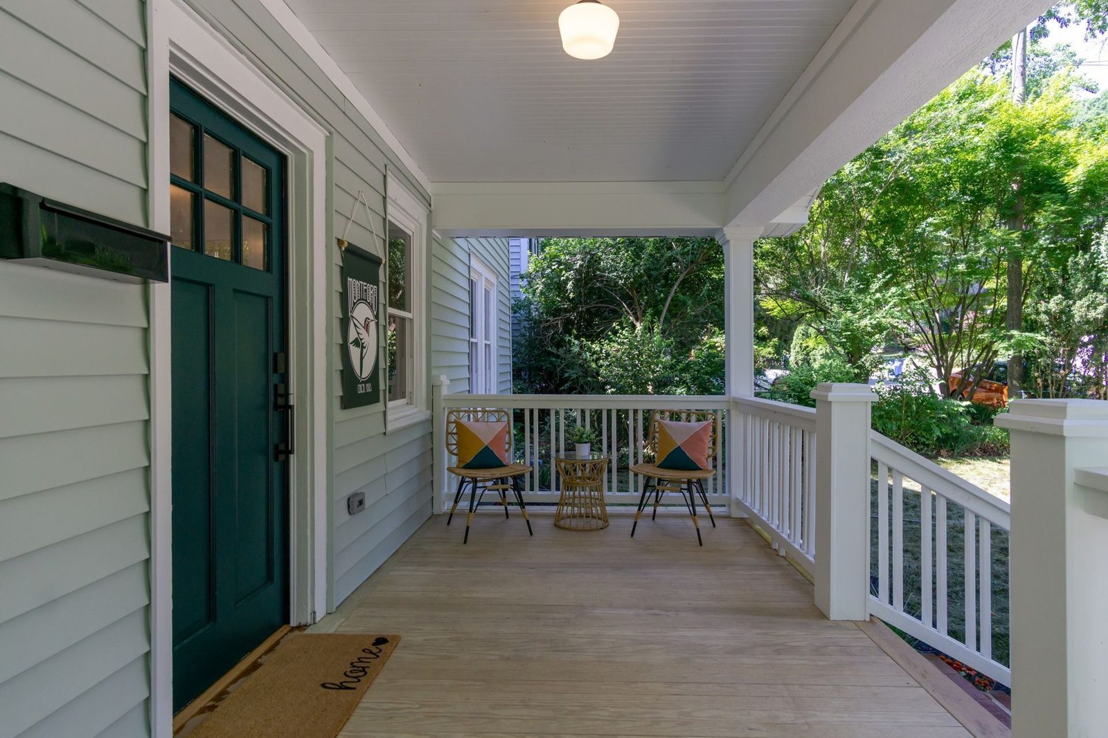 Covered front porch with a dark green door, white railings and porch chairs