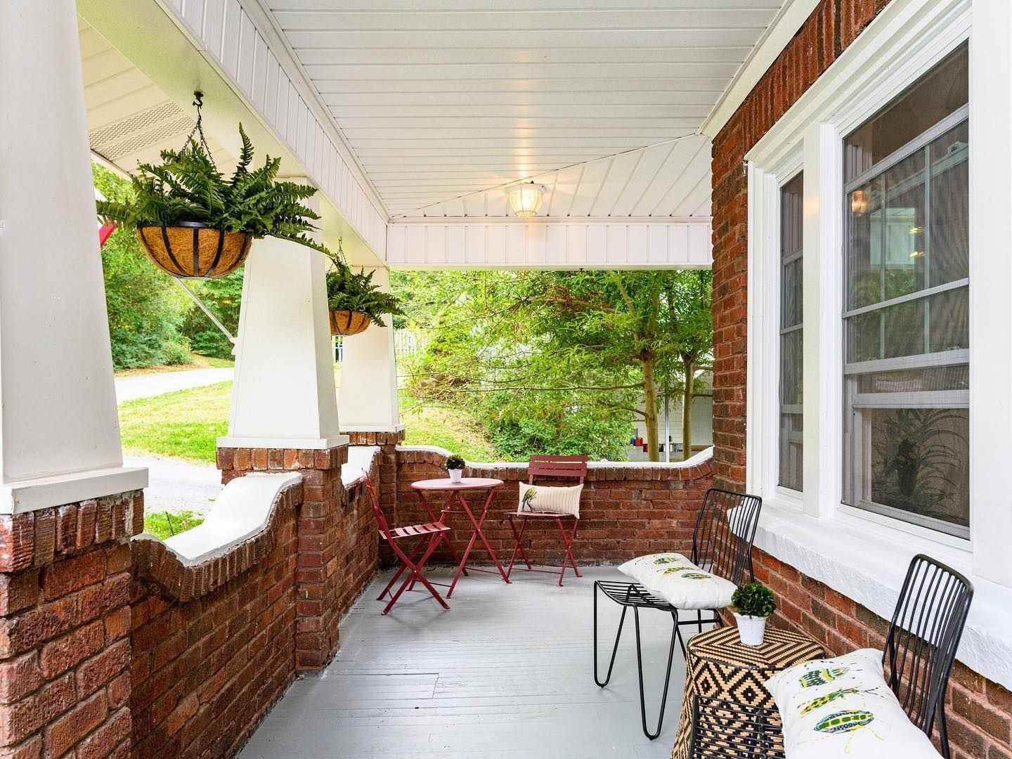 Brick porch with hanging ferns, a bistro table and seating