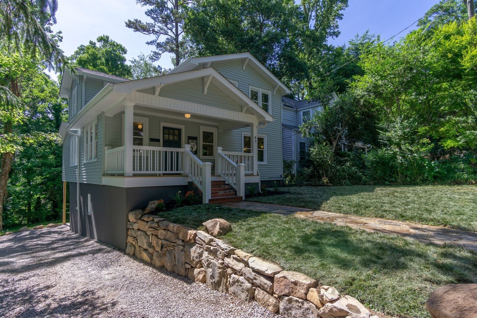 Gray bungalow with a white front porch above a stacked stone wall