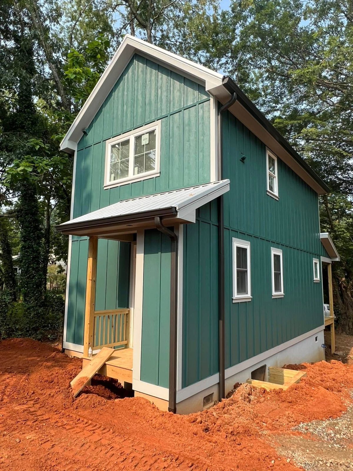Teal board-and-batten new home with a covered entry on freshly graded red clay