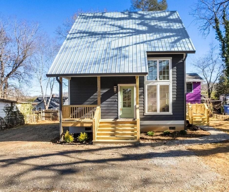 Small dark-sided cottage with a metal roof and a wood front porch
