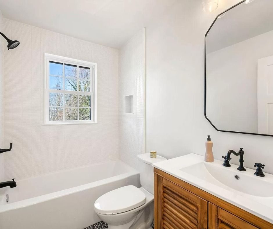 Bathroom with a wood vanity, an octagonal mirror and a tub