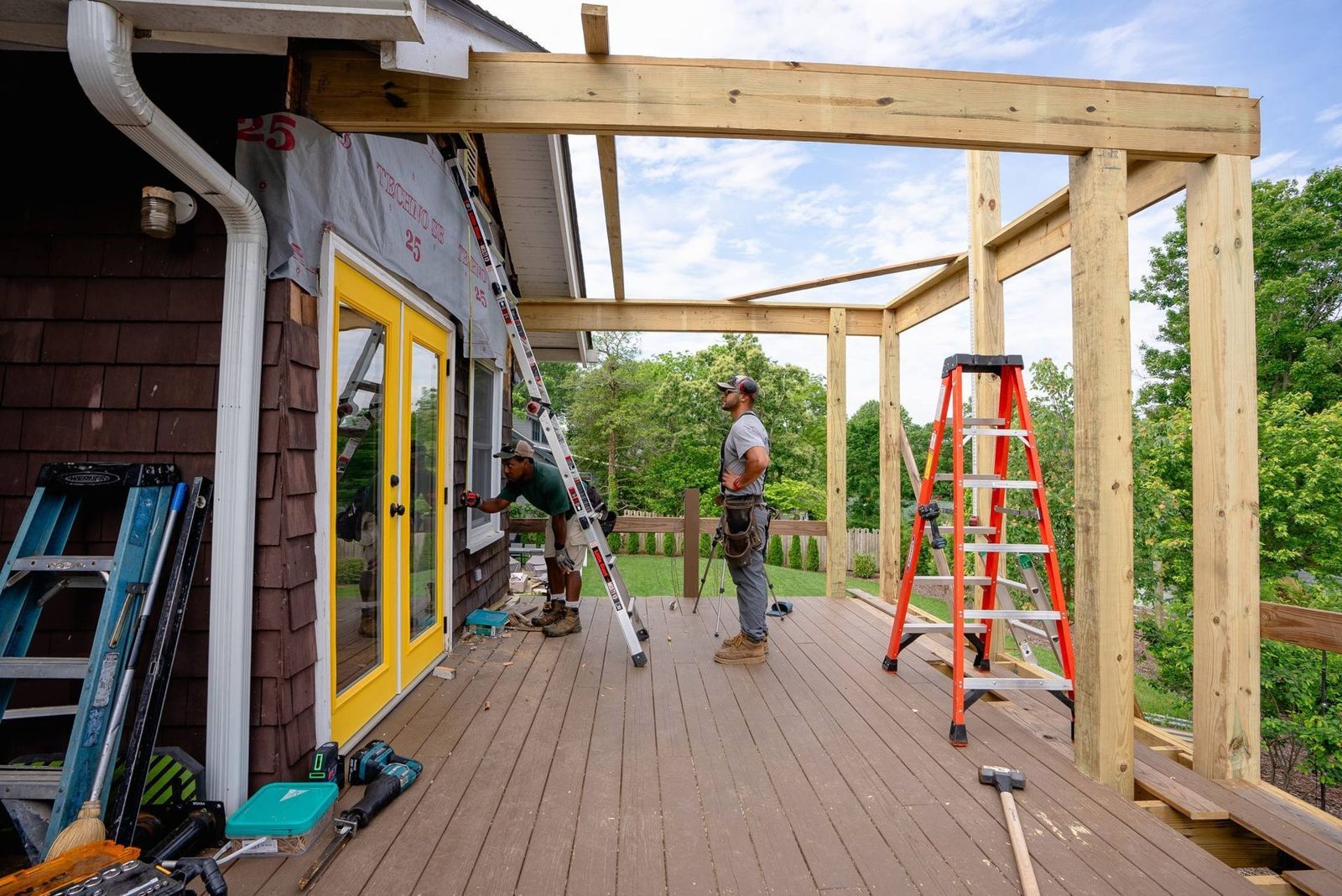Boundless crew framing a covered porch roof over a deck beside a yellow door