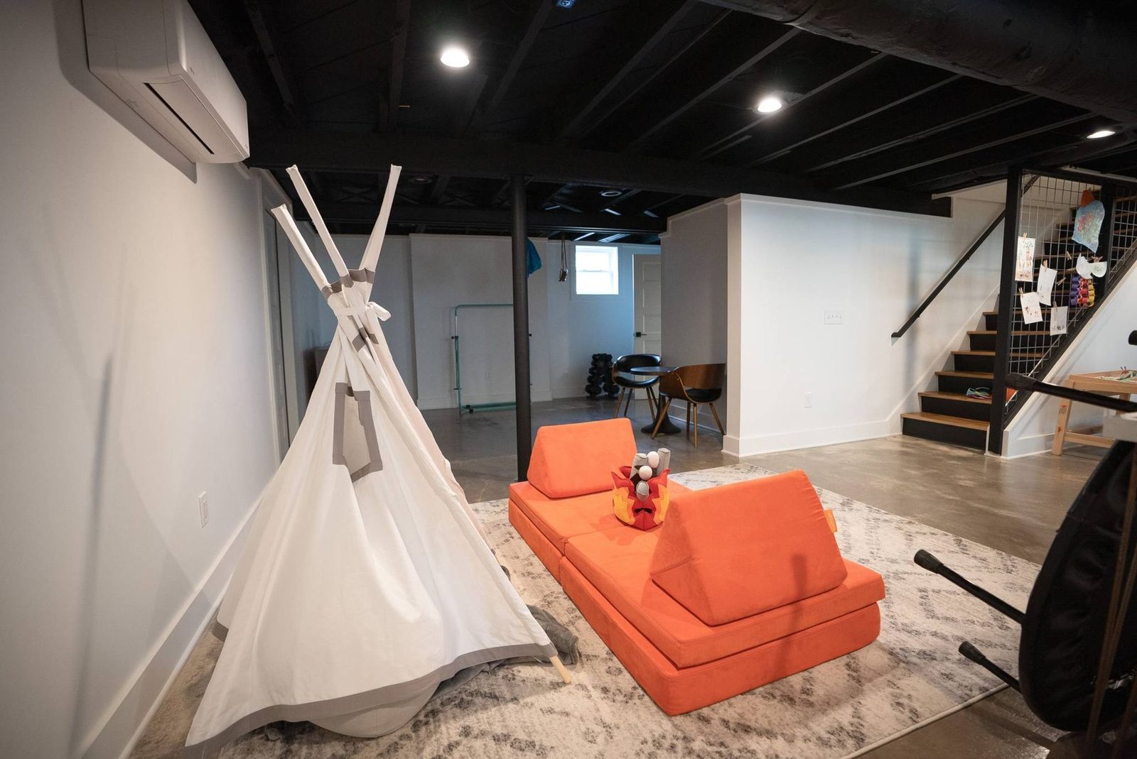 Basement play area with a teepee and orange lounge seating