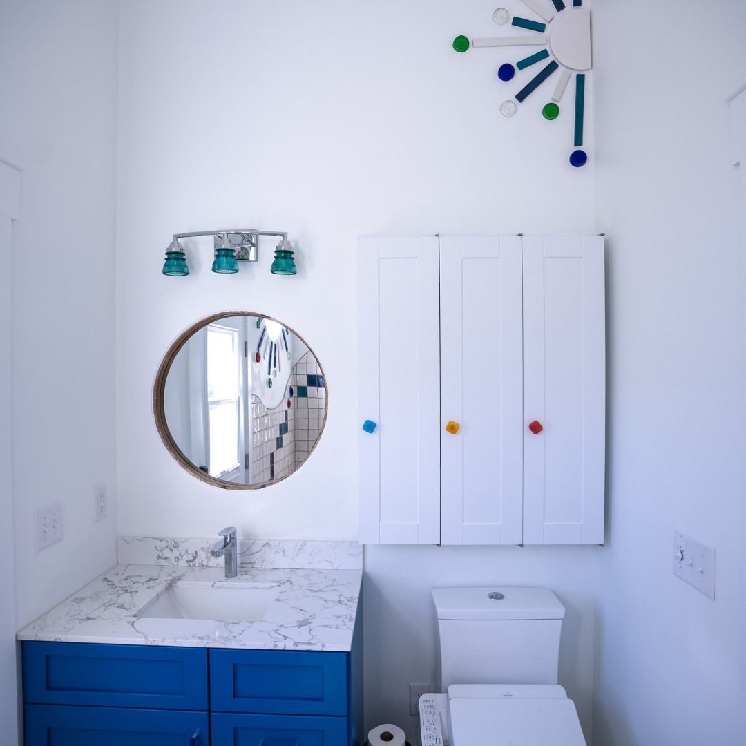 Bathroom with a blue vanity, a round mirror and colorful wall art