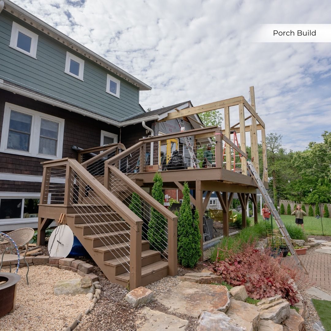 Multi-level wood deck with cable railings under construction behind a dark-sided house
