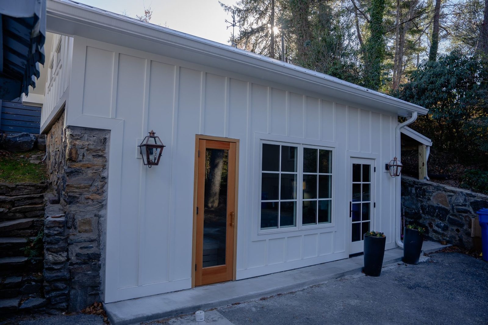 White board-and-batten building with stone retaining walls and glass doors