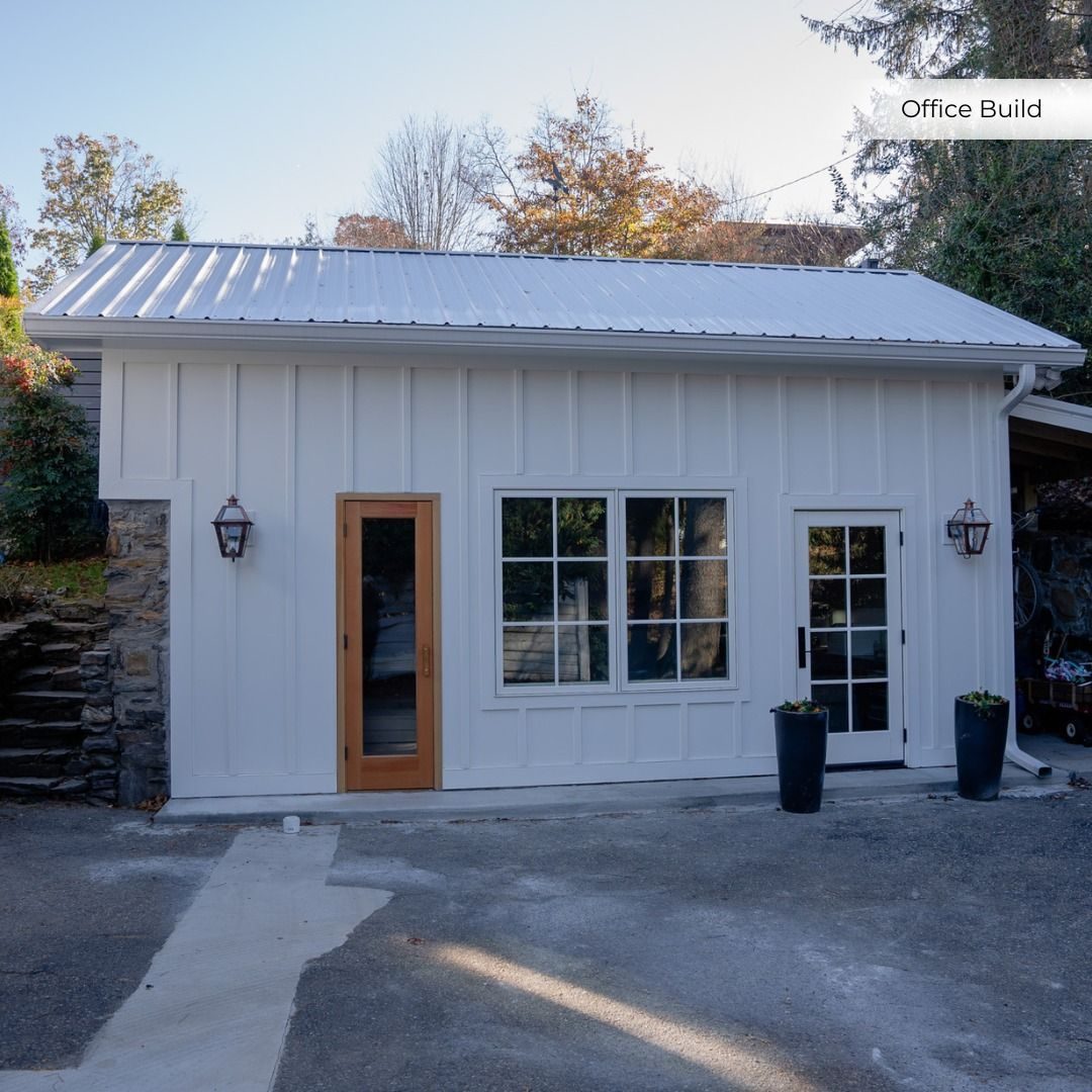 White board-and-batten office build with a wood-framed glass door and wall lanterns