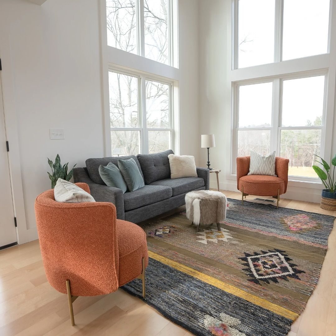 Two-story living room with tall windows, a gray sofa and orange accent chairs