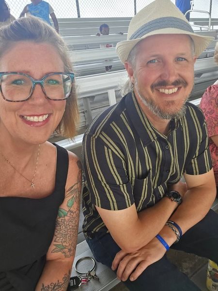 Billy and Christi Adams smiling outdoors, Billy in a straw hat
